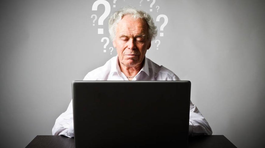 Senior man uses laptop surrounded by graphic question marks 