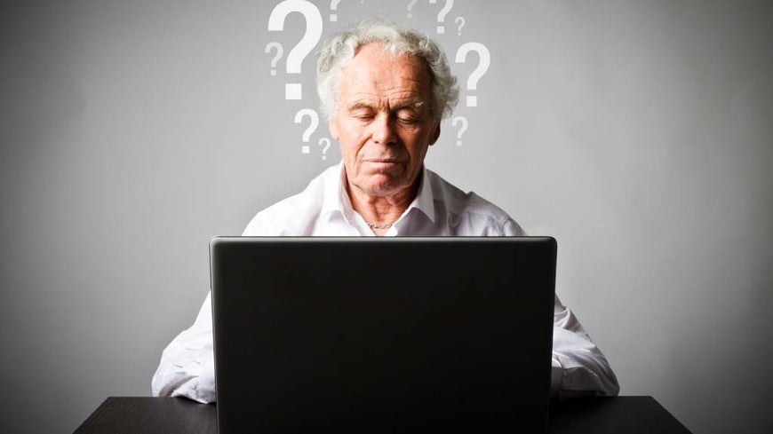 Senior man uses laptop surrounded by graphic question marks