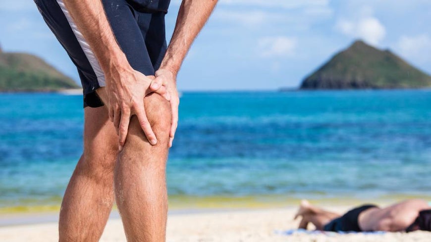 A senior suffering from knee pain in beach setting.