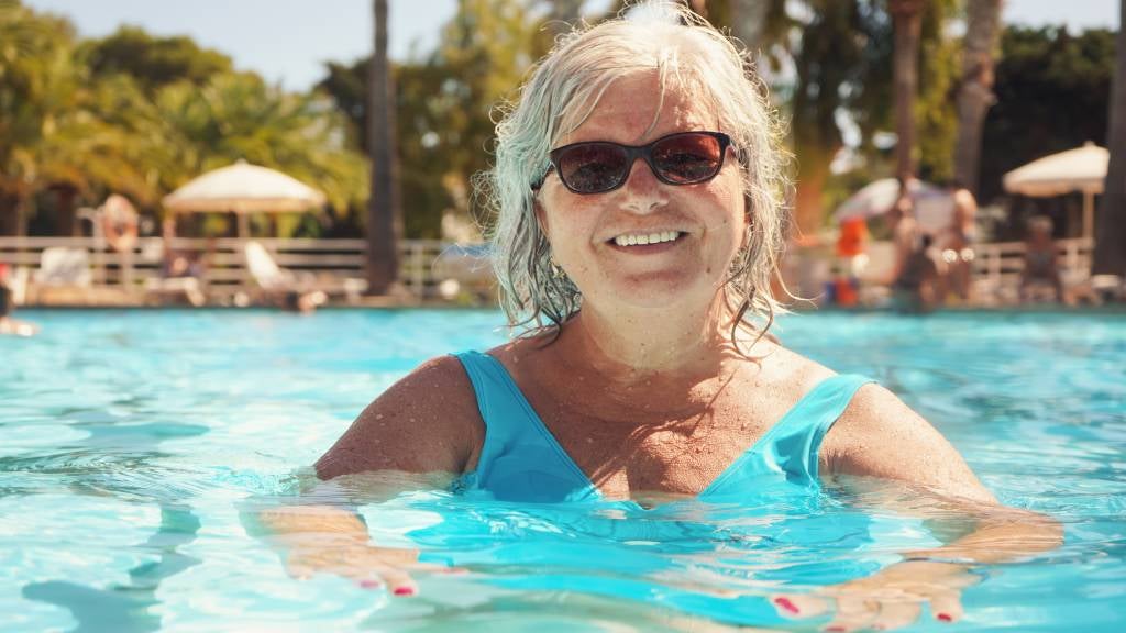 Woman in blue swimming costume floats in resort style pool