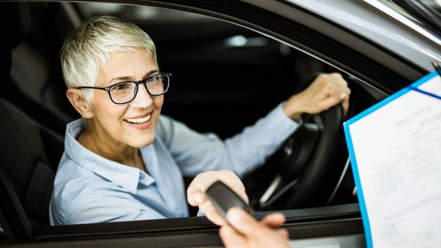 Happy senior woman taking her new car keys from sales person