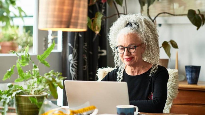 Senior woman with curly hair works on laptop