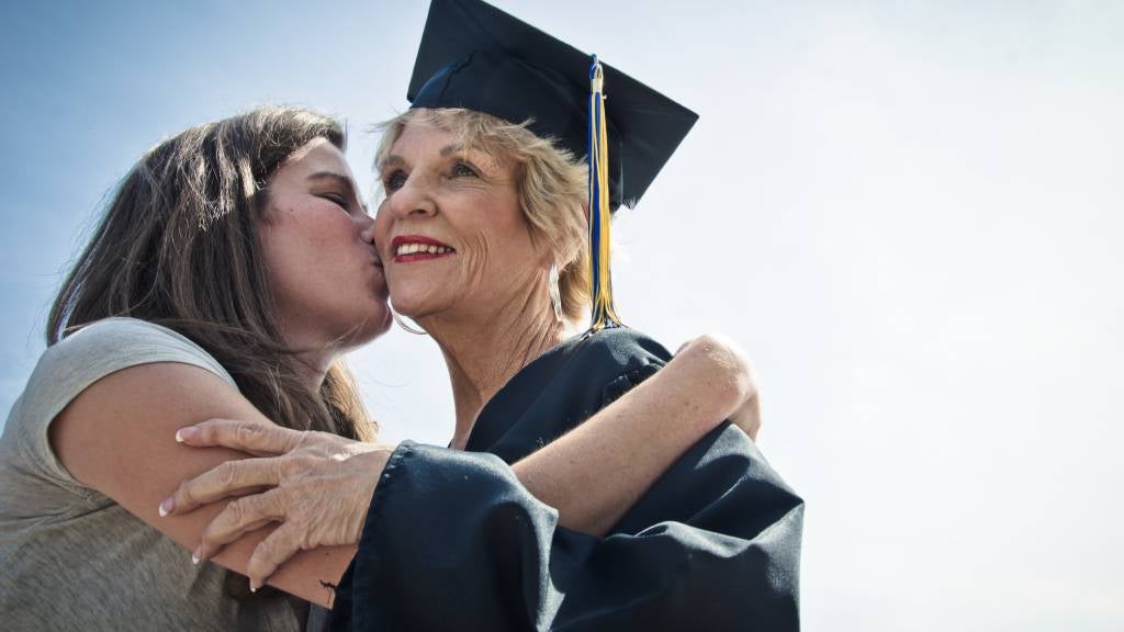 Senior woman graduates university. She is kissed on the check by young relative.