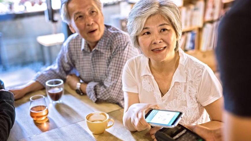 Older couple use smartphone in contactless cash payment at a café.