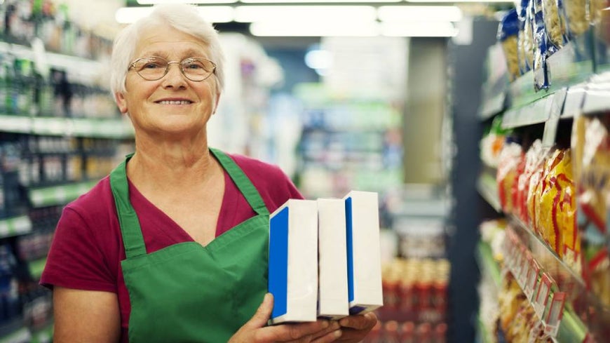 Senior woman works at a supermarket in green apron. 
