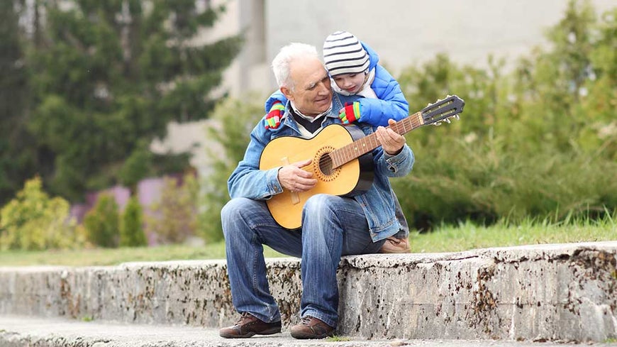 grandfather plays guitar to grandson in the park 