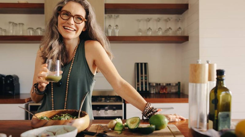 Senior woman smiles, surrounded by healthy foods in her kitchen. 