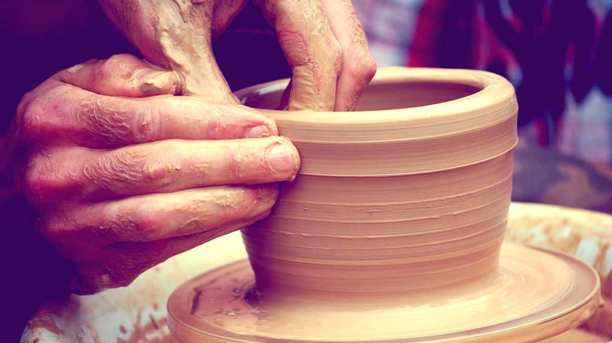 Person making clay pot on pottery wheel.