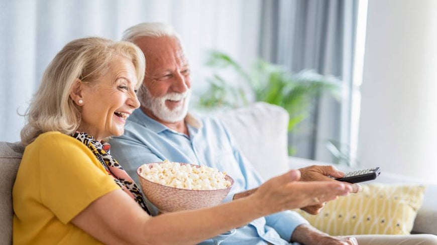 Happy senior couple watching a movie together in the lounge room