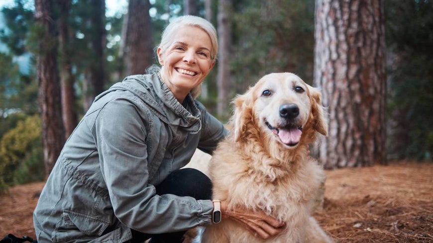 Senior woman with Golden Retriever in woodland setting