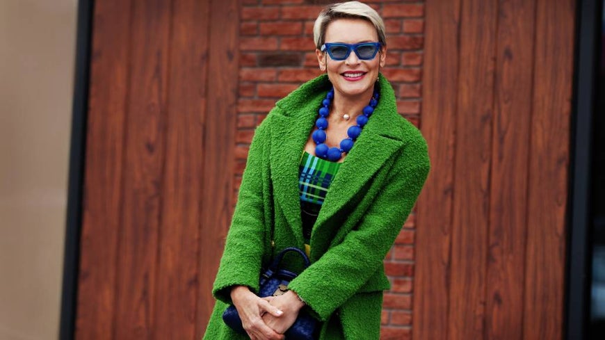 Senior woman in bright fashion, with green coat and blue beads.