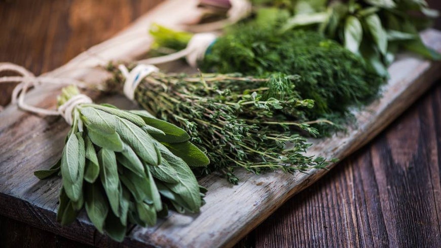 FRESH HERBS TIED WITH STRING ON A WOODEN CHOPPING BLOCK