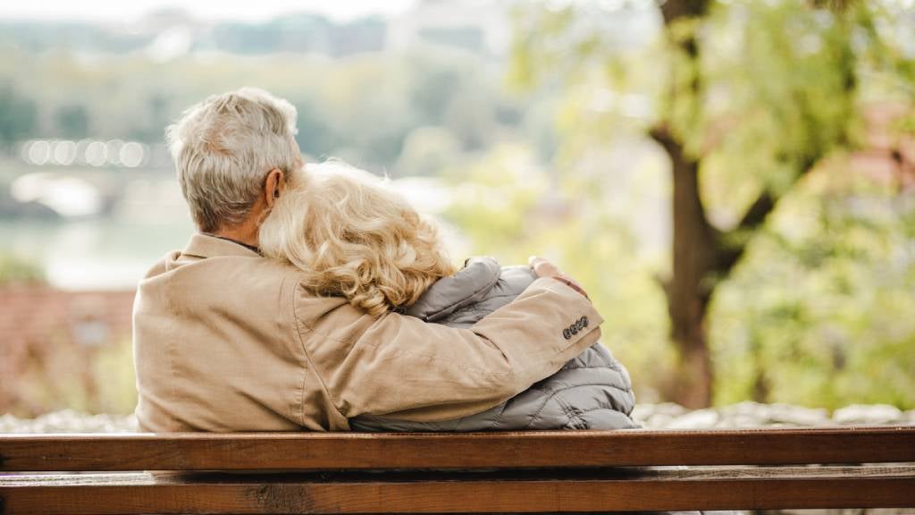 Older couple from behind sitting on a park bench.
