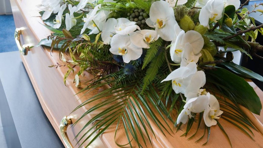 A white and green floral arrangement on top of a coffin