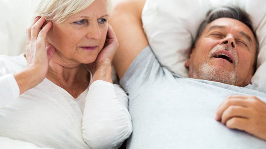 Senior man snoring and woman covering ears.