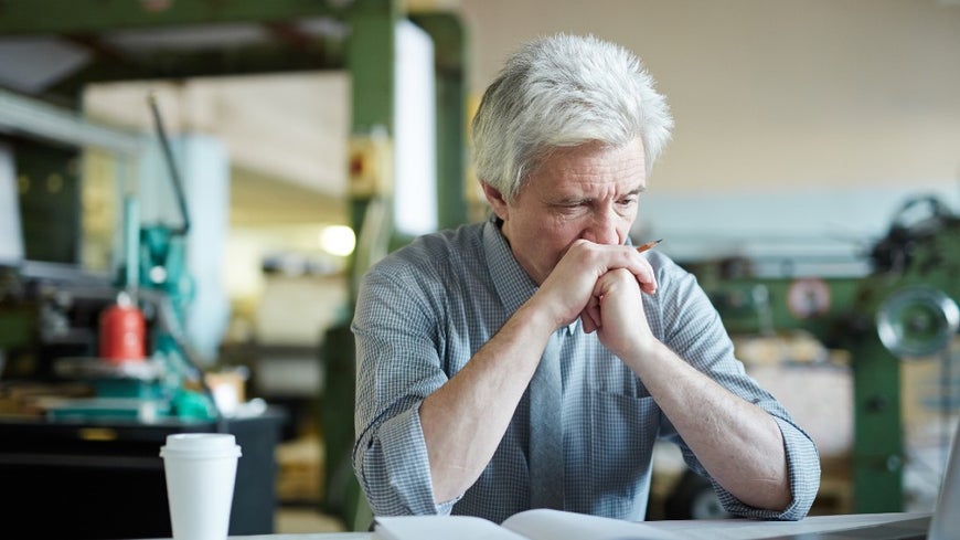 Senior man sitting down concentrating on his notebook with a pencil in hand. 