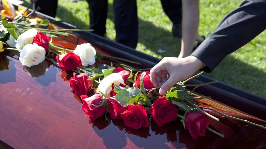 Person wearing black places rose onto a wooden coffin. 