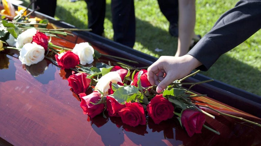 Person wearing black places rose onto a wooden coffin.