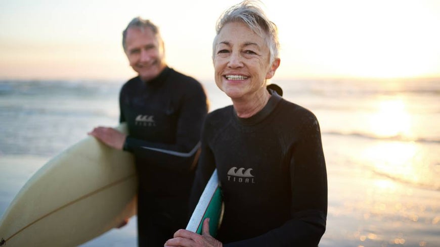 Senior man and woman on the beach in wetsuits with surf boards