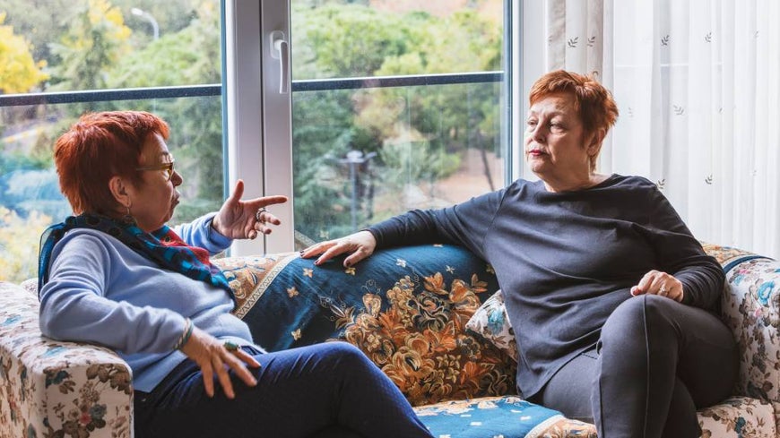 Two senior women argue politely sitting on a couch