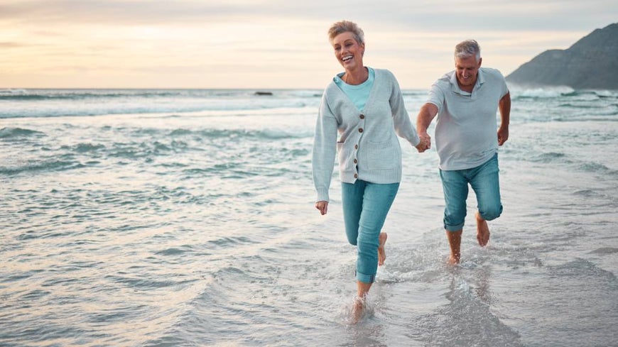 A happy senior couple walks along a beach at dusk. 