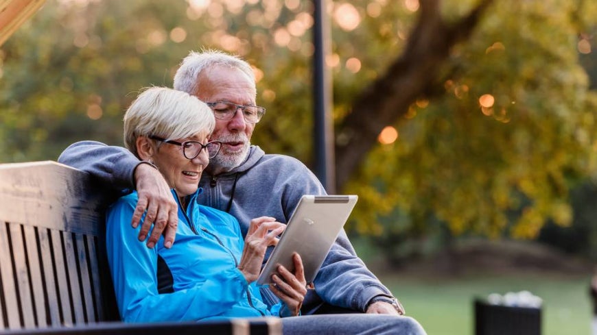 A happy couple sitting on a park bench using a tablet