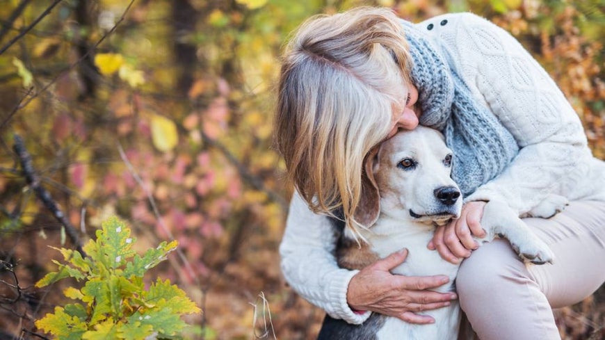 Senior woman hugs her dog in forest setting 