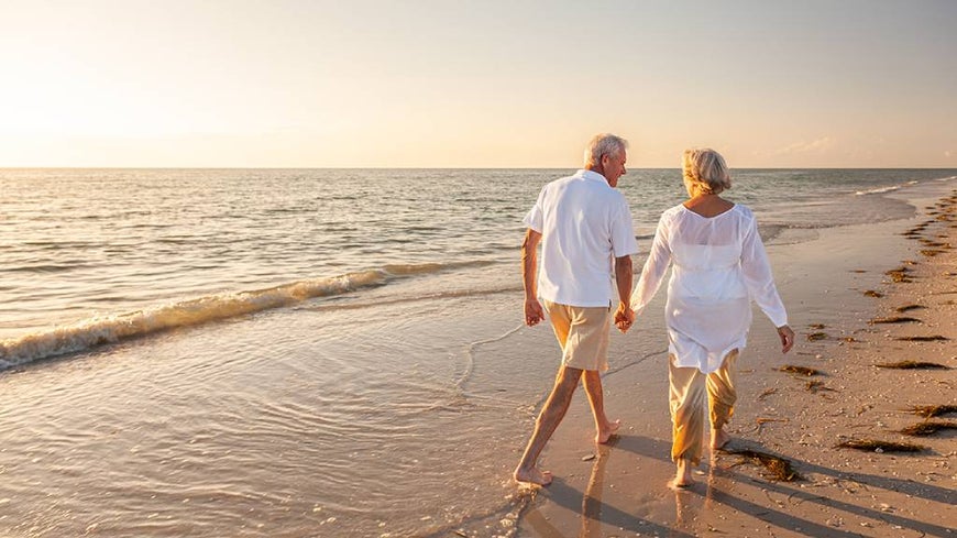 A senior couple walks along a beach at sunset