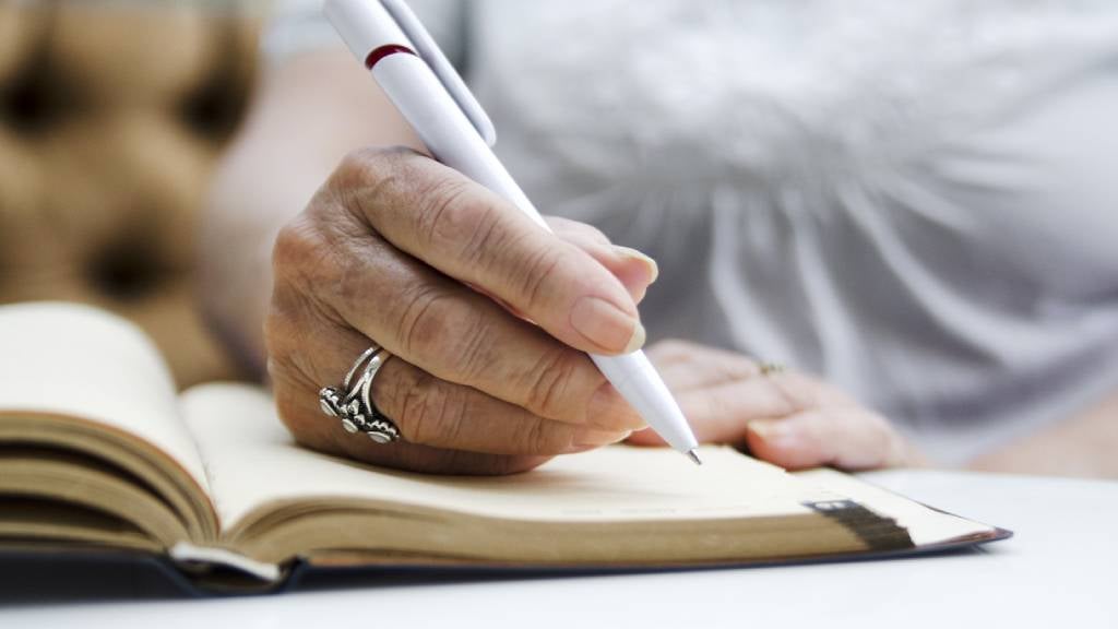 Senior woman with silver ring writes in her diary.