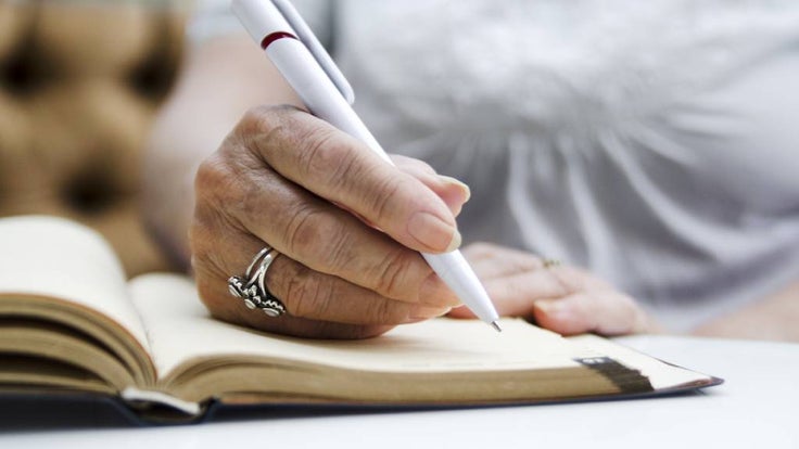Senior woman with silver ring writes in her diary. 