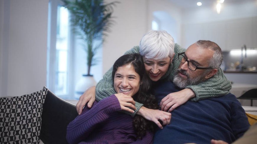 Adult daughter embraces senior parents in their home. 