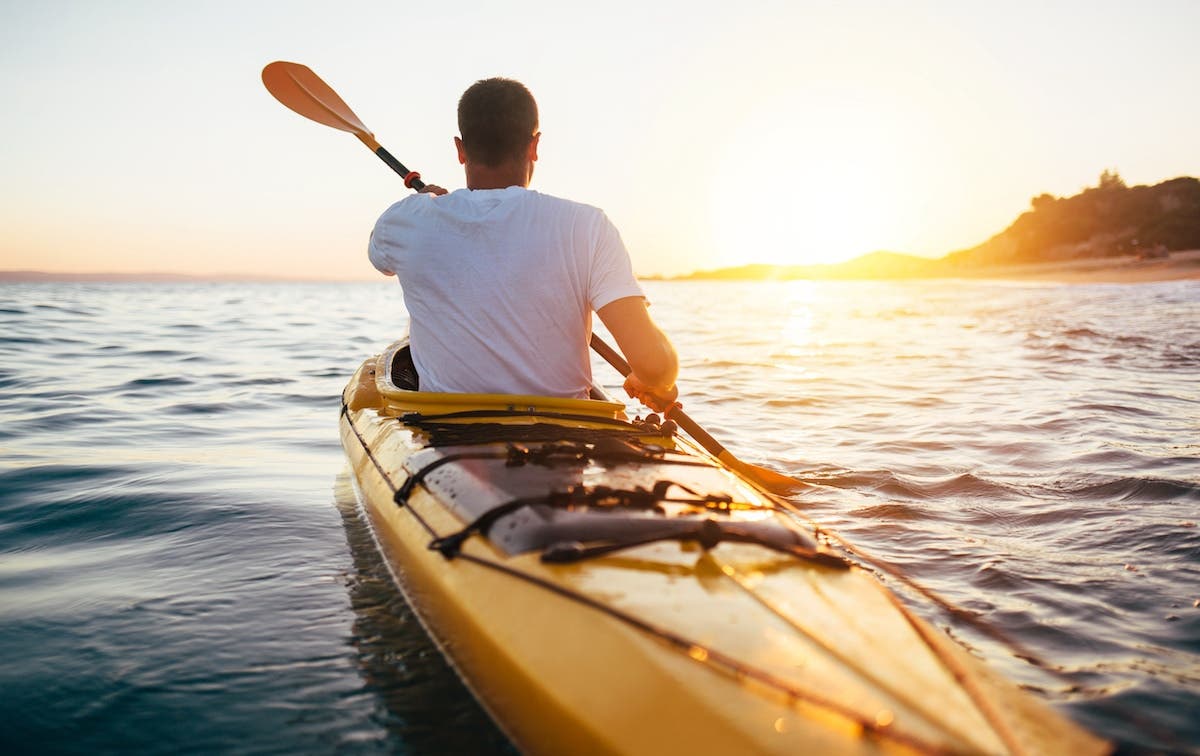 Guy on a canoe at sunrise, paddling in water