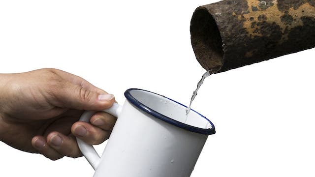 Water pouring into a tin cup, coming out of an old rusted pipe 