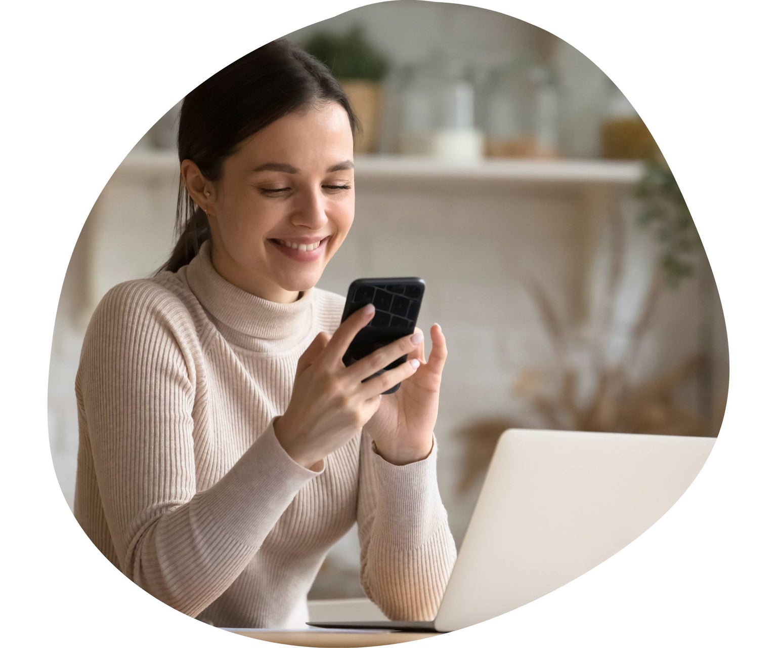 woman smiling on phone next to laptop at home