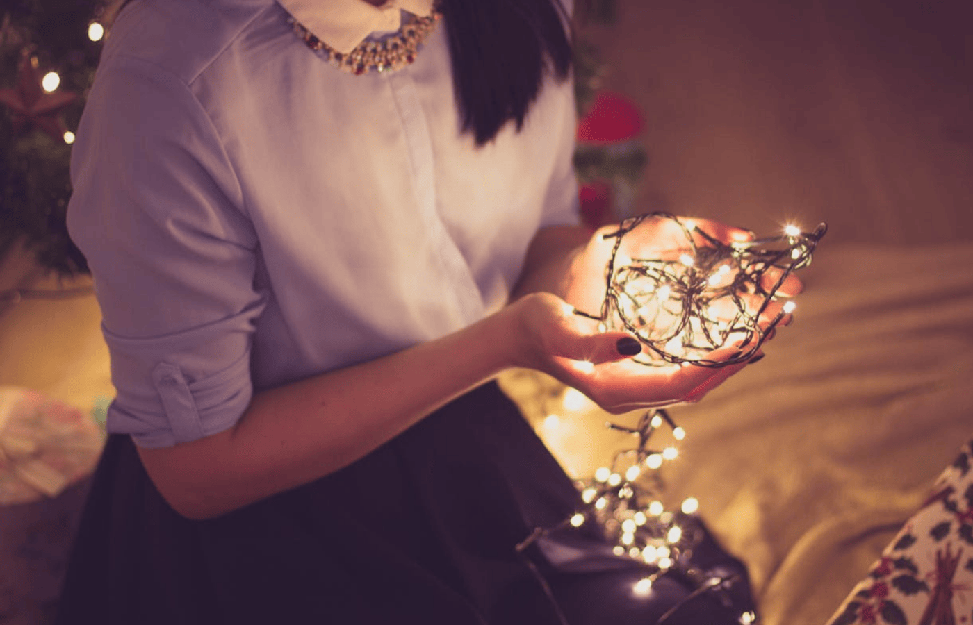 A close up of a woman's hands. She is holding Christmas lights.