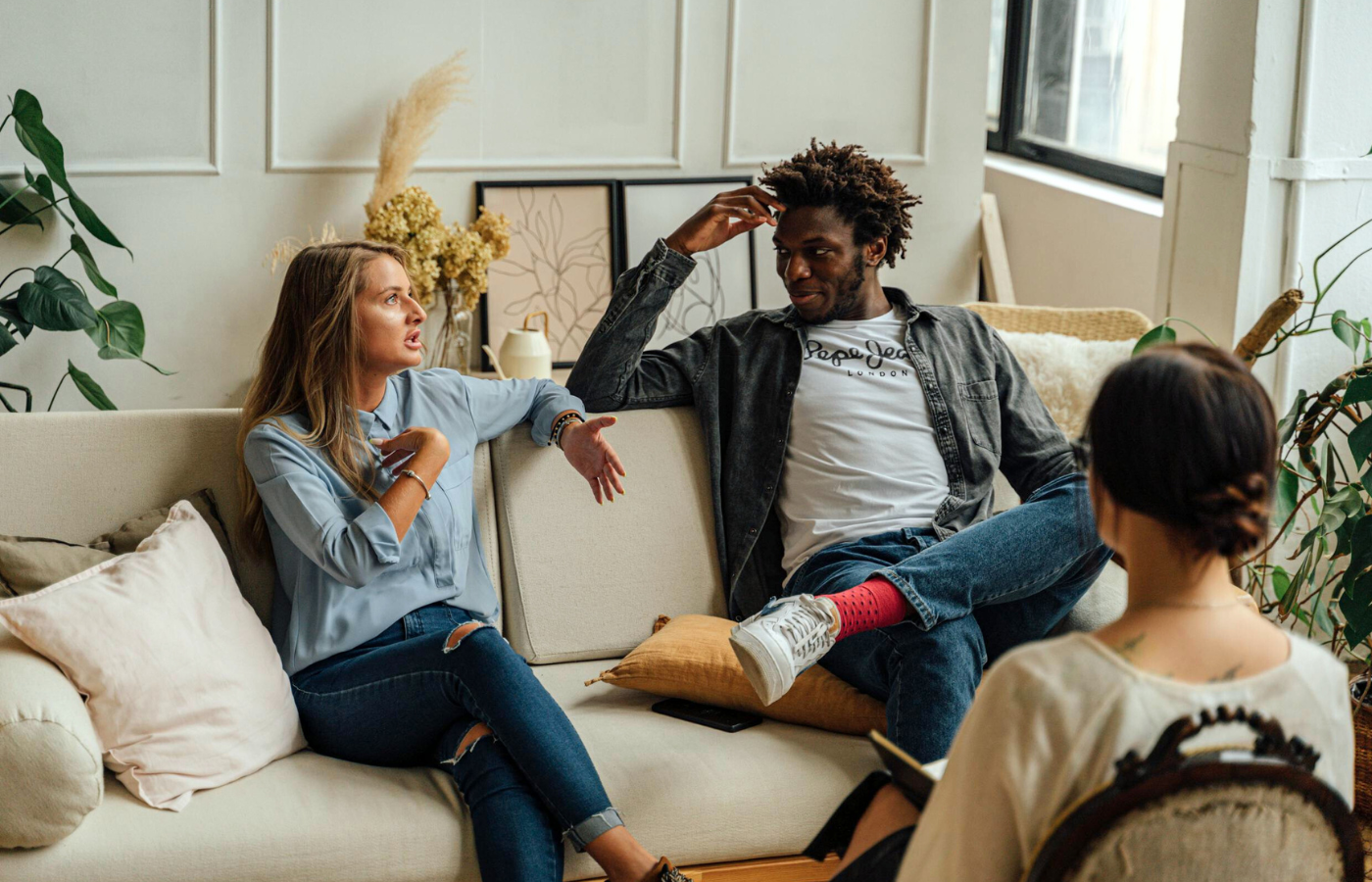 A full shot of a couple (a man and woman) and their their couples therapist. The woman is speaking, while her partner and the therapist listen attentively.