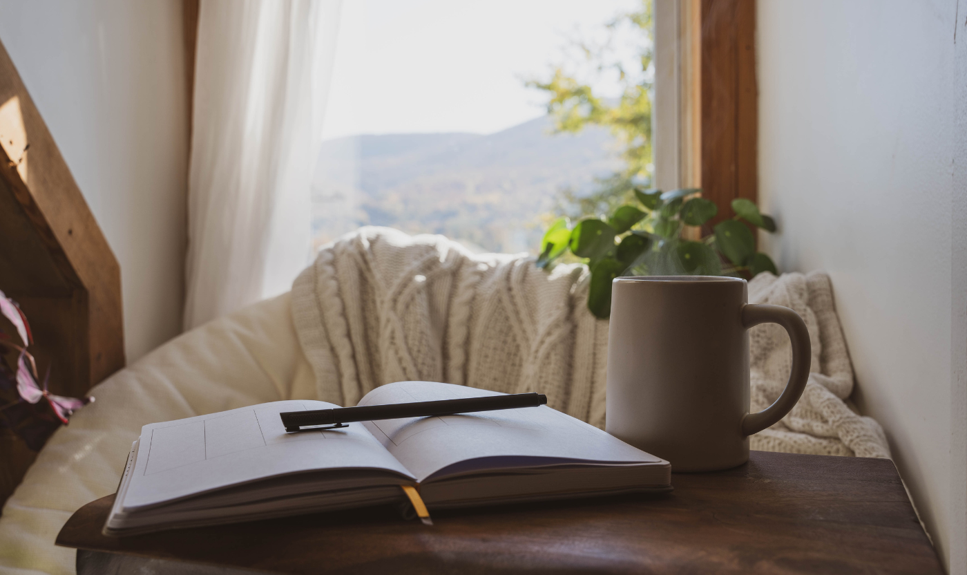 An open journal and mug sit by a cosy window, inviting reflection and self-care. This scene supports mental health after pregnancy loss.
