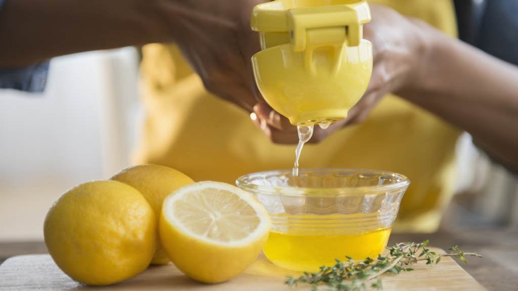 Lemons getting squeezed into a bowl using a lemon squeezer.