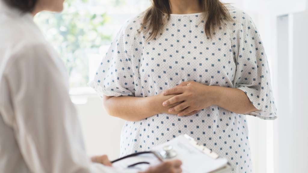 Woman in a hospital gown receiving check up from doctor.