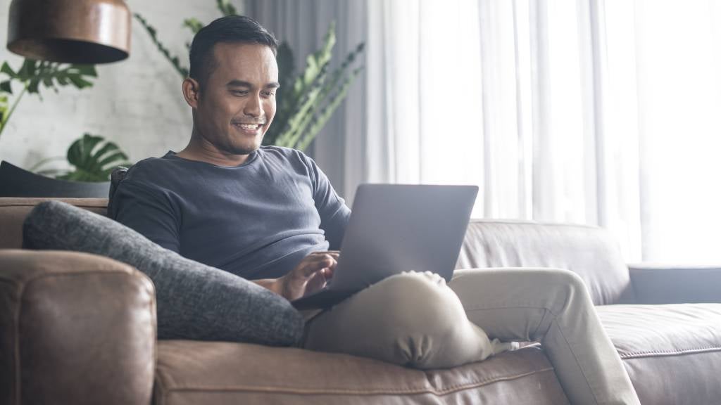 Man sitting on couch with laptop smiling.