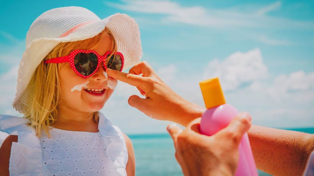 Mother applying sunscreen to daughter’s nose at the beach.