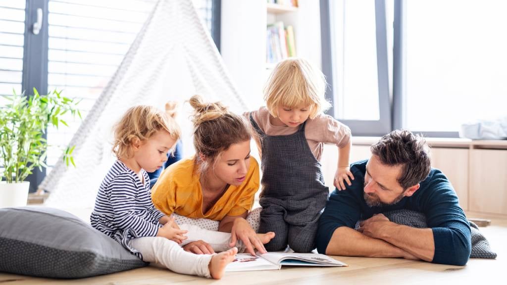 Young family with two small children indoors reading a book together