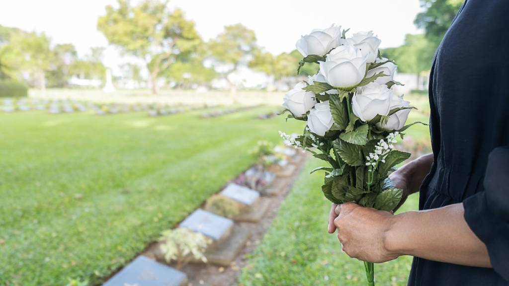 Mourning woman hold rose bouquet near stone gravestites