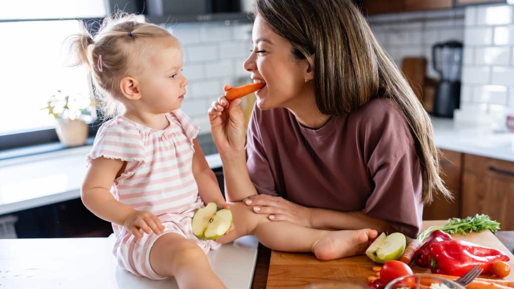 Woman and child eating veggies in the kitchen