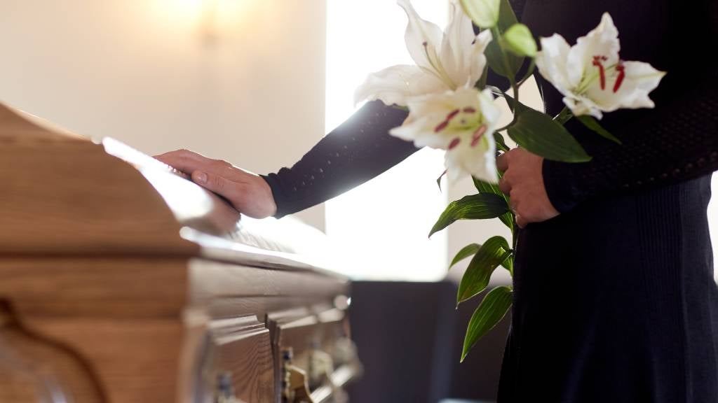 Woman standing at coffin with flowers at funeral