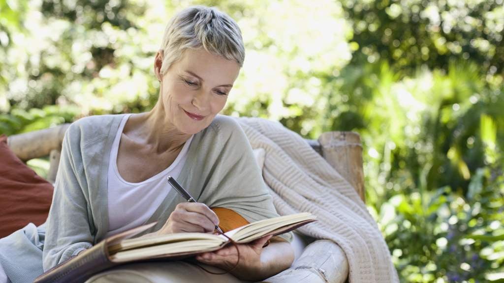 Woman sitting in chair writing in notebook while smiling