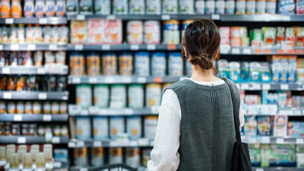 Woman grocery shopping looking at items on the shelf.