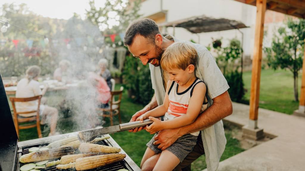 Happy father and son smiling while they bbq corn in their backyard for family lunch.