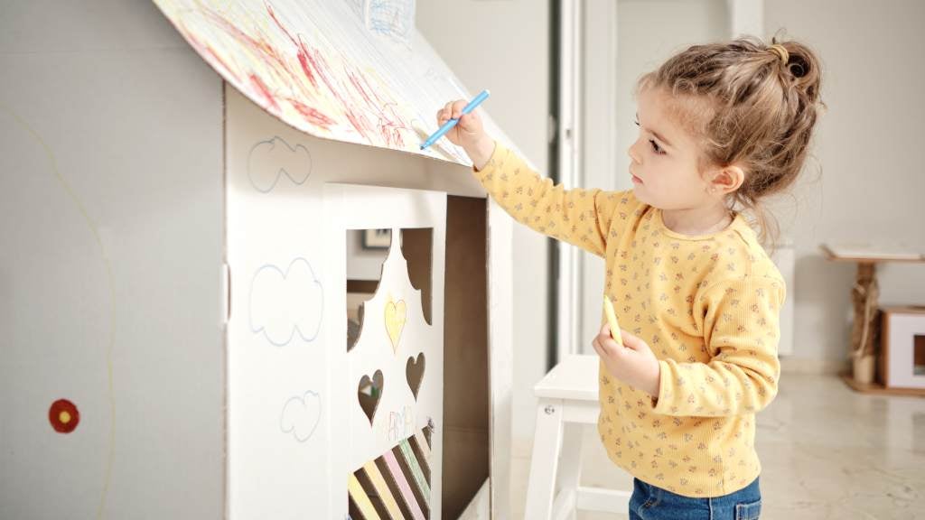 Little girl colouring in a cardboard cubby house