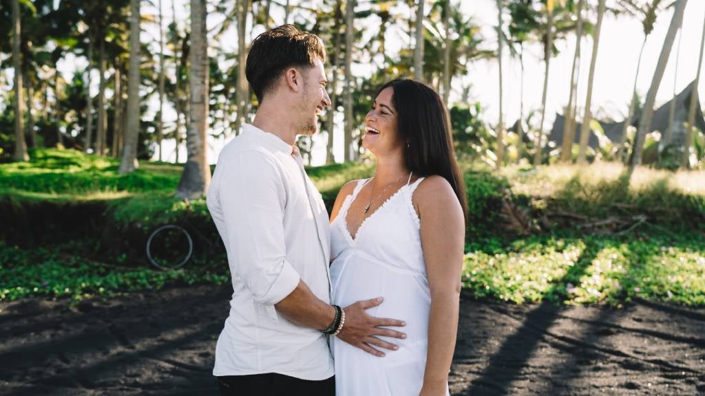 Pregnant couple on beach laughing together